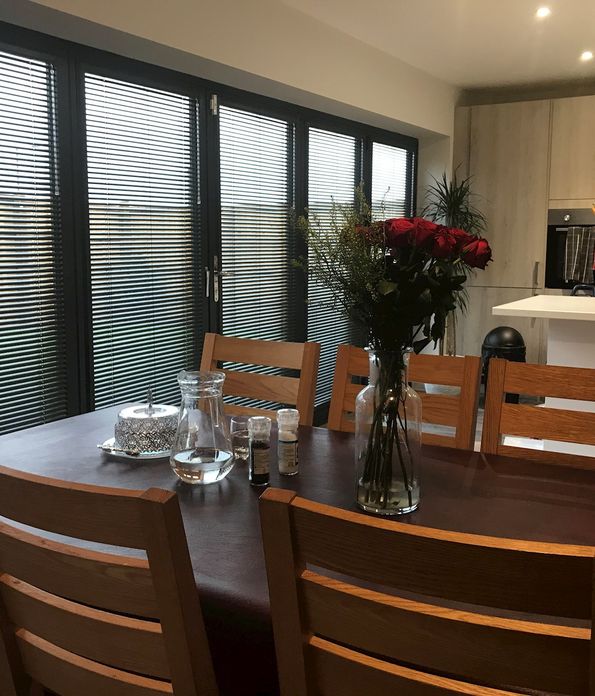 perfect fit metal venetian blinds on bifold doors in kitchen with dark brown dining table