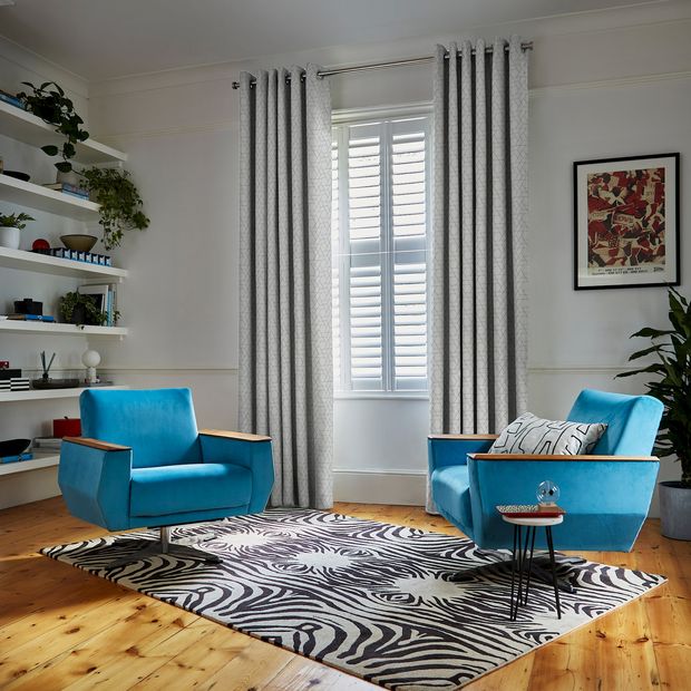 jive blue curtains in white lounge with vibrant blue armchairs, black and white rug, and small table