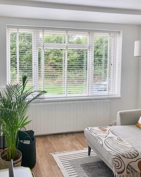 white wooden blinds on large window in bedroom with rug covered wooden floors