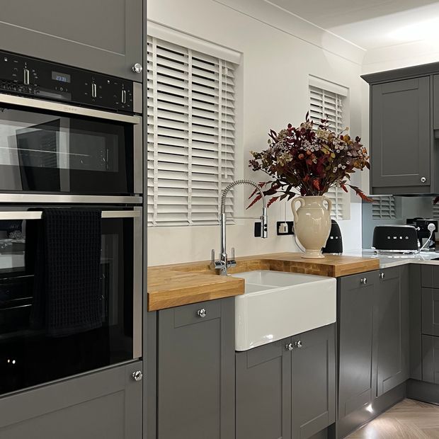 pair of plain white wooden blinds on small windows in modern silver/grey themed kitchen with wooden countertops
