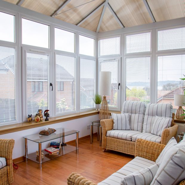 white metal venetian blinds on side windows in large conservatory with rattan furniture