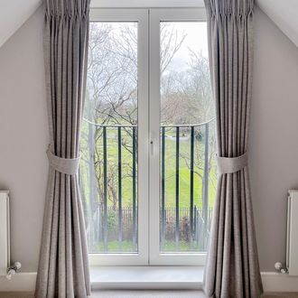 cream plain textured floor length curtains covering french doors with matching tie backs