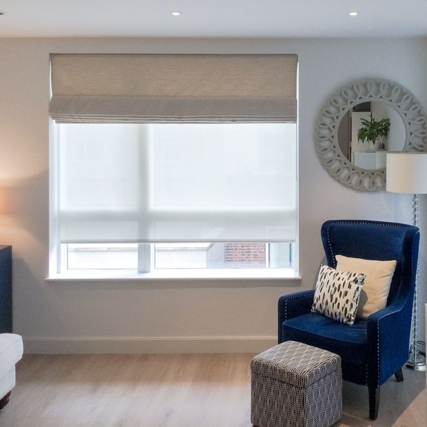 cream roman blind paired with white roller blind on large window in living room with blue armchair