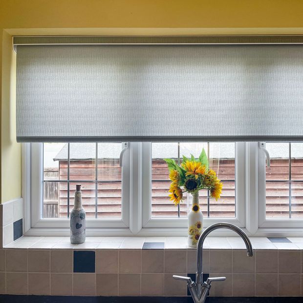 light grey slightly speckled roller blind on large window above kitchen sink