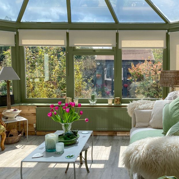 set of beige roller blinds on conservatory side windows surrounded by greenery