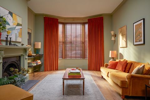 orange curtains paired with brown faux wooden blinds on large bay window in cosy living room with light orange furniture