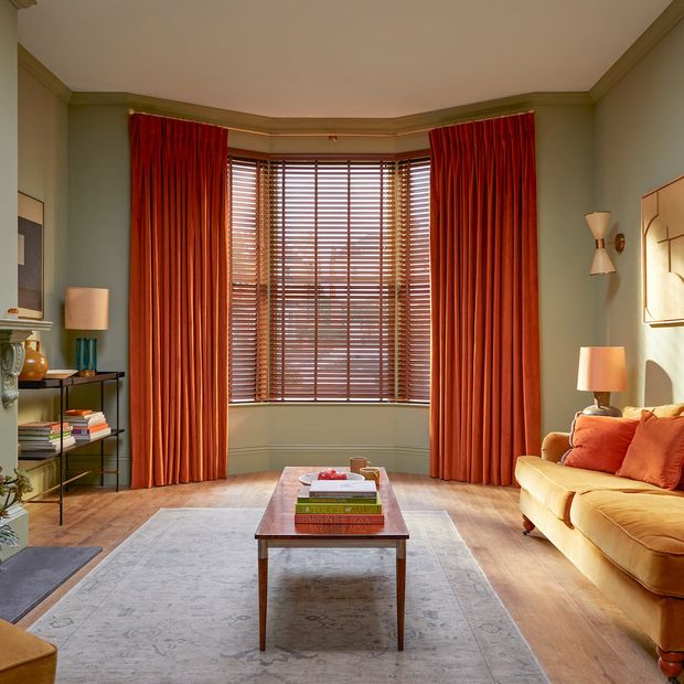 orange curtains paired with brown faux wooden blinds on large bay window in cosy living room with light orange furniture