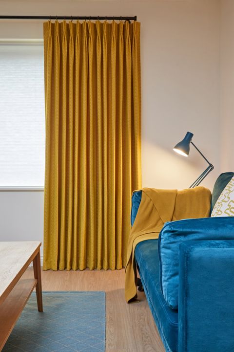yellow floor length curtains paired with light pleated blinds in living room with blue sofa