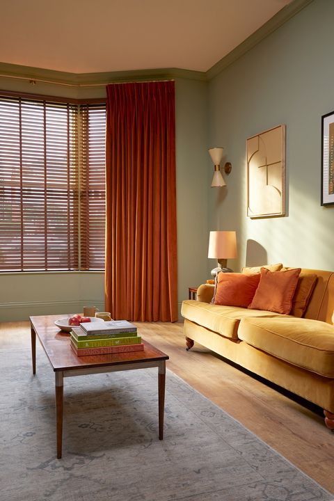 burnt orange floor length curtains on wide bay window paired with wooden blinds in living room