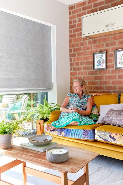 Woman sat on sofa next to large window covered by grey roman blinds