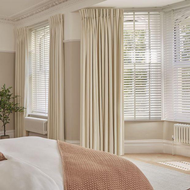 cream curtains paired with white wooden blinds on bay windows in cosy elegant bedroom