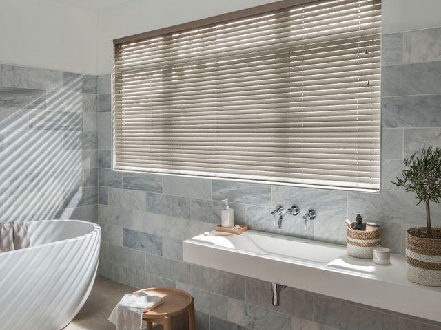 Hillarys Faux Wood Venetian Shades in a Dusk Bathroom covering a large white bath