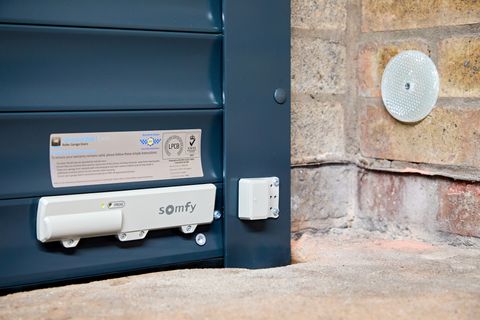 Close up of the bottom of a grey garage door, showing a somfy motor, locking system and a secured by design plaque.