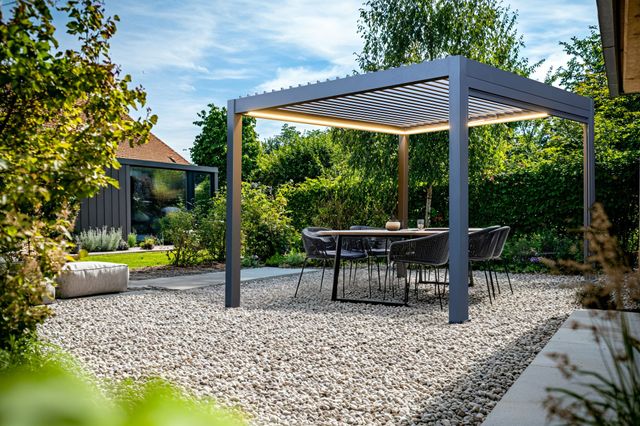 Garden exterior with shinge patio with a freestanding grey pergola with fabric roof over four chairs and a table.