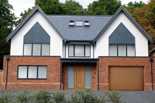 Large contemporary two-tone house with apex windows and integral garage with light brown door matching front door.