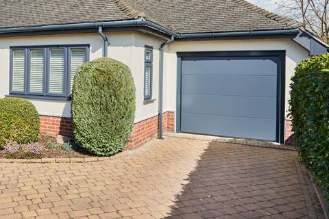 Corner shot of single storey house in white with anthracite grey integral sectional garage door matching guttering and window frames and block paved driveway.