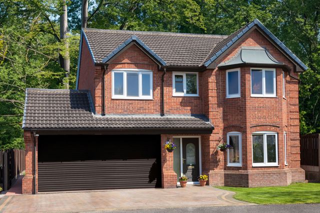 Large traditional brick house with apex windows and double internal garage with dark brown roller door that matches the front door.