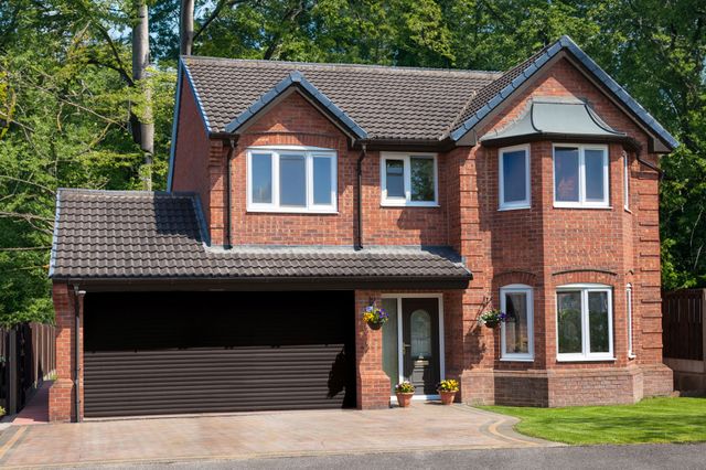 Large traditional brick house with apex windows and double internal garage with dark brown roller door that matches the front door.