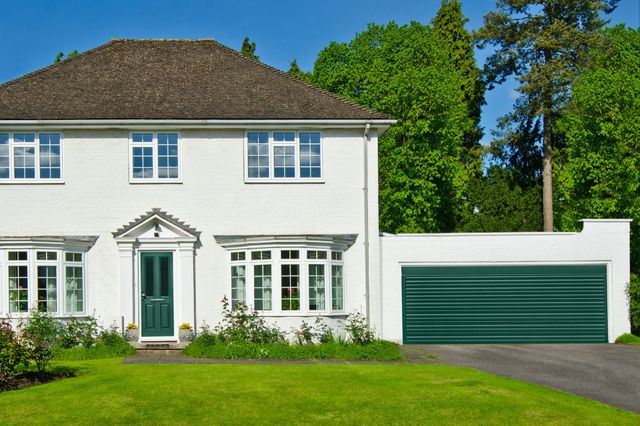 Large white house with bay windows, green door and attached garage in matching white with green door.