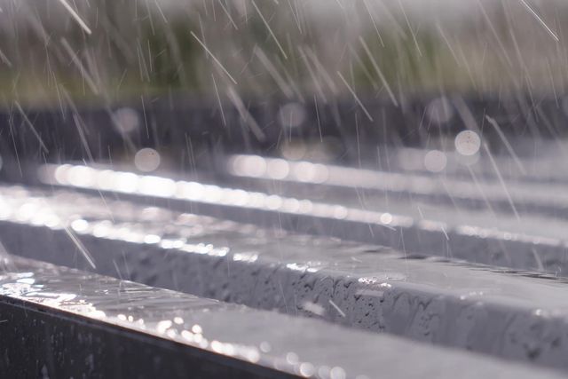 Heavy rain on a grey louvred roof of an aluminium pergola.