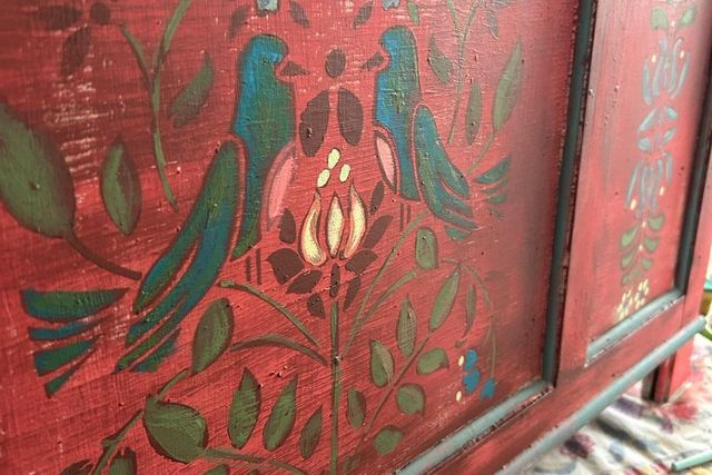 Close up of front of a painted wooden unit, with motif of pair of facing birds surrounded by flowers on a mid red background.