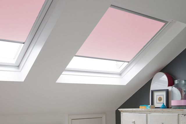 White room with white painted floorboards, white chest of drawers, white modern rocking chair and skylight window to eaves dressed in soft pink roller blinds.