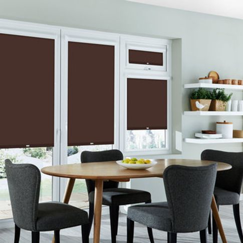 multiple dark brown coloured roller blinds fitted to windows in a dining room with a wooden dining table and fabric chairs