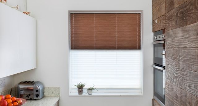Brown venetian blinds paired with white transition blinds on a rectangular window in a kitchen decorated with white and wood tones